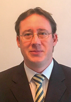 Formális öltözet, sötét öltöny, fehér ing és csíkos nyakkendő látható a képen.