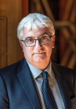 Elegánsan öltözött férfi sötét öltönyben és pöttyös nyakkendővel, háttérben faajtó.