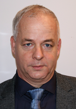 Egy férfi elegáns öltözetben, sötétkék ingben és kockás nyakkendőben.