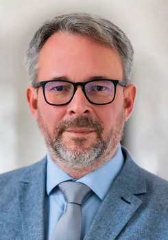 Középkorú férfi elegáns öltönyben és nyakkendőben.