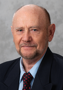 Idős férfi elegáns öltönyt visel, kék kockás inggel és piros mintás nyakkendővel.