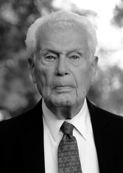 Elegáns öltönyben lévő férfi, fehér inggel és mintás nyakkendővel, fekete-fehér képen.