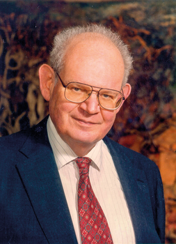 Elegánsan öltözött férfi sötétkék öltönyben, fehér csíkos ingben és piros mintás nyakkendővel.