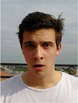 Fiatal férfi fehér pólóban, háttérben városi táj látható.