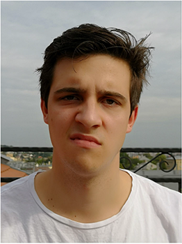 Fiatal férfi fehér pólóban, háttérben városi táj látható.