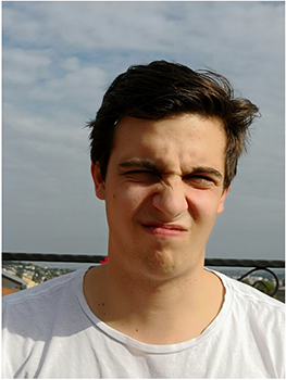 Fiatal férfi fehér pólóban, háttérben városi táj látható.