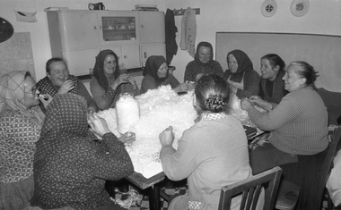 Nők csoportja tollat foszt egy asztal körül ülve, hagyományos közösségi munka.