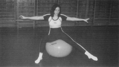 Nő fitnesz labdán tornateremben Egy nő fitnesz labdán ül, karjait oldalra kinyújtva egy tornateremben.