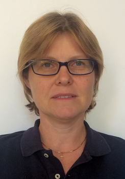 Egy személy arany kereszt medálos nyakláncot visel, sötétkék galléros pólóban.