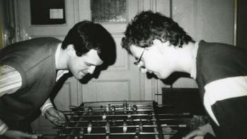 Két ember asztali focit játszik egy beltéri helyiségben, koncentrálva a játékra.