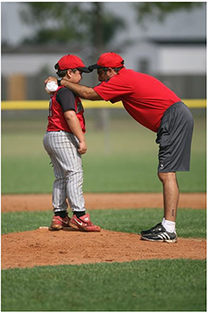Baseball edző tanácsot ad a fiatal játékosnak Baseball edző tanácsot ad a fiatal játékosnak a pályán, piros mezben és sapkában.