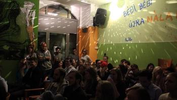 Beltéri esemény emberekkel és feliratokkal a falon Beltéri esemény, ahol emberek ülnek és állnak egy szobában, falon feliratok és dekorációk.