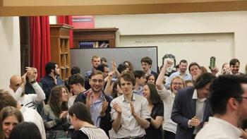 Csoport emberek beltéri rendezvényen, könyvespolcok és feliratok a háttérben.