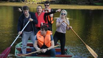 Csapat evezés közben egy csónakban Öt ember evez egy csónakban, ketten mentőmellényt viselnek.