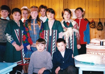 Csoport hagyományos népviseletben egy kulturális eseményen Csoport hagyományos népviseletben, háttérben falra akasztott dísztárgyak és asztalon hagyományos edények.