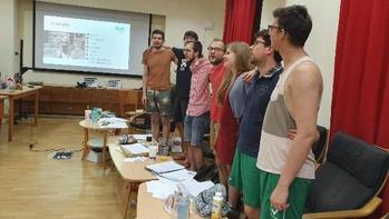 Csoport ember egy teremben, háttérben kivetítőn diavetítés látható.