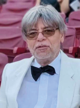 Elegáns férfi fehér zakóban és fekete csokornyakkendőben Elegáns öltözetű férfi fehér zakóban és fekete csokornyakkendőben, háttérben piros székekkel