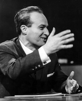 Elegáns öltönyben lévő férfi gesztikulál a kezével, beszéd közben.