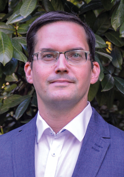 Elegáns öltönyben lévő személy fehér ingben, zöld növényekkel a háttérben