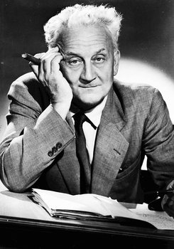 Elegáns öltönyben lévő személy szivarral, asztalnál ülve, előtte papírok.