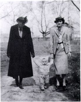 Elegáns felnőttek és gyermek sétálnak vidéken Két felnőtt és egy kisgyermek sétál egy vidéki úton, elegáns ruhában, kopár fák között.