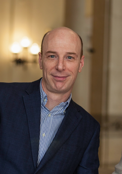 Elegáns férfi sötétkék zakóban és kockás ingben Elegáns öltözetű férfi sötétkék zakóban és kockás ingben, beltéri helyiségben, lámpák háttérben.