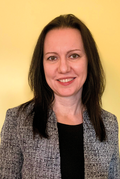 Elegáns nő szürke zakóban és fekete felsőben Egy nő elegáns szürke zakót visel fekete felsővel, háttérben sárga fal.