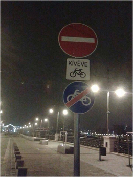 Ellentmondásos kerékpáros közlekedési tábla éjszaka Kerékpáros közlekedési tábla, amely ellentmondásos üzenetet közvetít: behajtani tilos, kivéve kerékpárosok, de kerékpáros közlekedési tilalom is látható.