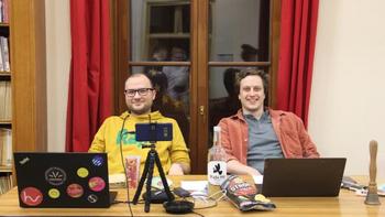 Két ember ül egy asztalnál laptopokkal és kamerával Két ember ül egy asztalnál, laptopokkal, kamerával és egy üveg itallal, chips az asztalon.