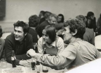 Emberek egy asztal körül beszélgetnek Csoport ember ül egy asztal körül, üvegek és poharak az asztalon.