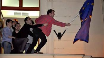 Emberek egy épület párkányán EU zászlóval Több ember áll egy épület párkányán, és egy EU zászlót tartanak.