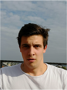 Fehér pólót viselő személy, háttérben felhős égbolt és városi táj látható.