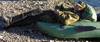 Férfi katonai ruhában fekszik egy gumicsónakban a kavicsos parton.