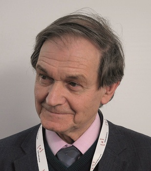 Férfi öltönyben, nyakkendővel és konferencia jelvénnyel a nyakában.