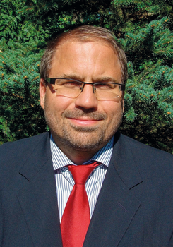 Férfi öltönyben piros nyakkendővel, zöld növényzet háttérrel