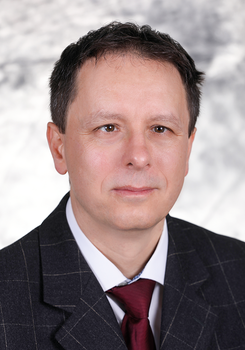 Férfi öltönyben, piros nyakkendővel, szürke mintás háttérrel