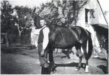 Férfi lóval vidéki ház előtt Egy férfi látható, aki egy lovat tart a kezében egy vidéki ház előtt.