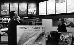 Férfi pékségben a pultnál, menüt tanulmányozva Férfi pékségben áll a pultnál, menüt tanulmányozza, eladóval beszélget.