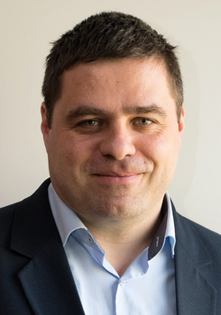 Férfi sötét öltönyben és világoskék ingben, arca elhomályosítva