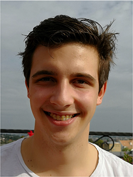 Fiatal férfi fehér pólóban, háttérben városi táj látható