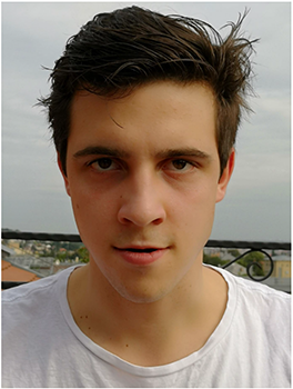 Fiatal férfi fehér pólóban, háttérben városi táj látható.