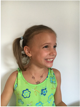 Fiatal lány zöld, virágmintás ruhát visel, haját copfba kötve.