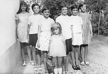 Fiatal lányok csoportképe fekete-fehérben Hét fiatal lány áll egy lépcsőn különböző ruhákban, fekete-fehér fotó, homályos arcok.