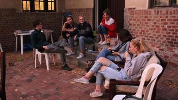 Fiatalok beszélgetnek egy udvaron Fiatalok ülnek és beszélgetnek egy udvaron, téglafal mellett.