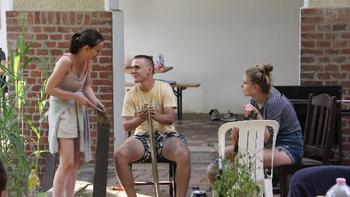 Fiatalok beszélgetnek egy udvaron Három fiatal beszélget és pihen egy udvaron, székek és növények között.