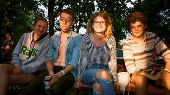 Fiatalok ülnek egy padon a parkban Négy fiatal ül egy padon egy parkban vagy erdős területen, lazán öltözve.