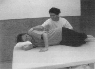 Fizikoterápiás kezelés fekvő személyen Terapeuta fizikoterápiás gyakorlatot végez egy fekvő személyen terápiás asztalon.