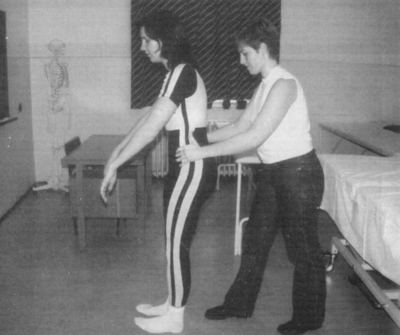 Fizioterápiás gyakorlat segítséggel egy orvosi környezetben Két ember, egyikük segíti a másikat egy gyakorlat végrehajtásában egy orvosi környezetben, háttérben csontváz.