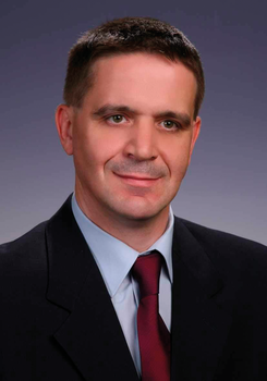 Formális öltözet, amely egy sötét öltönyből, világoskék ingből és bordó nyakkendőből áll.