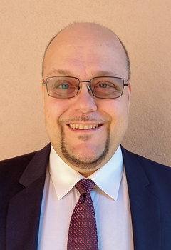 Formális öltözet, amely sötét zakóból, fehér ingből és mintás nyakkendőből áll.